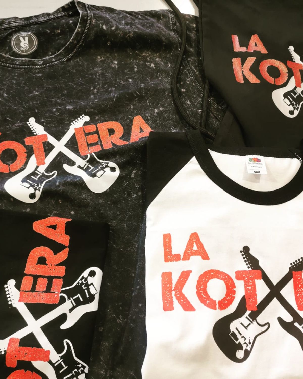 Camisetas personalizadas con el logo "La Kotxera", diseño de guitarras eléctricas cruzadas y letras rojas sobre fondo negro y blanco.