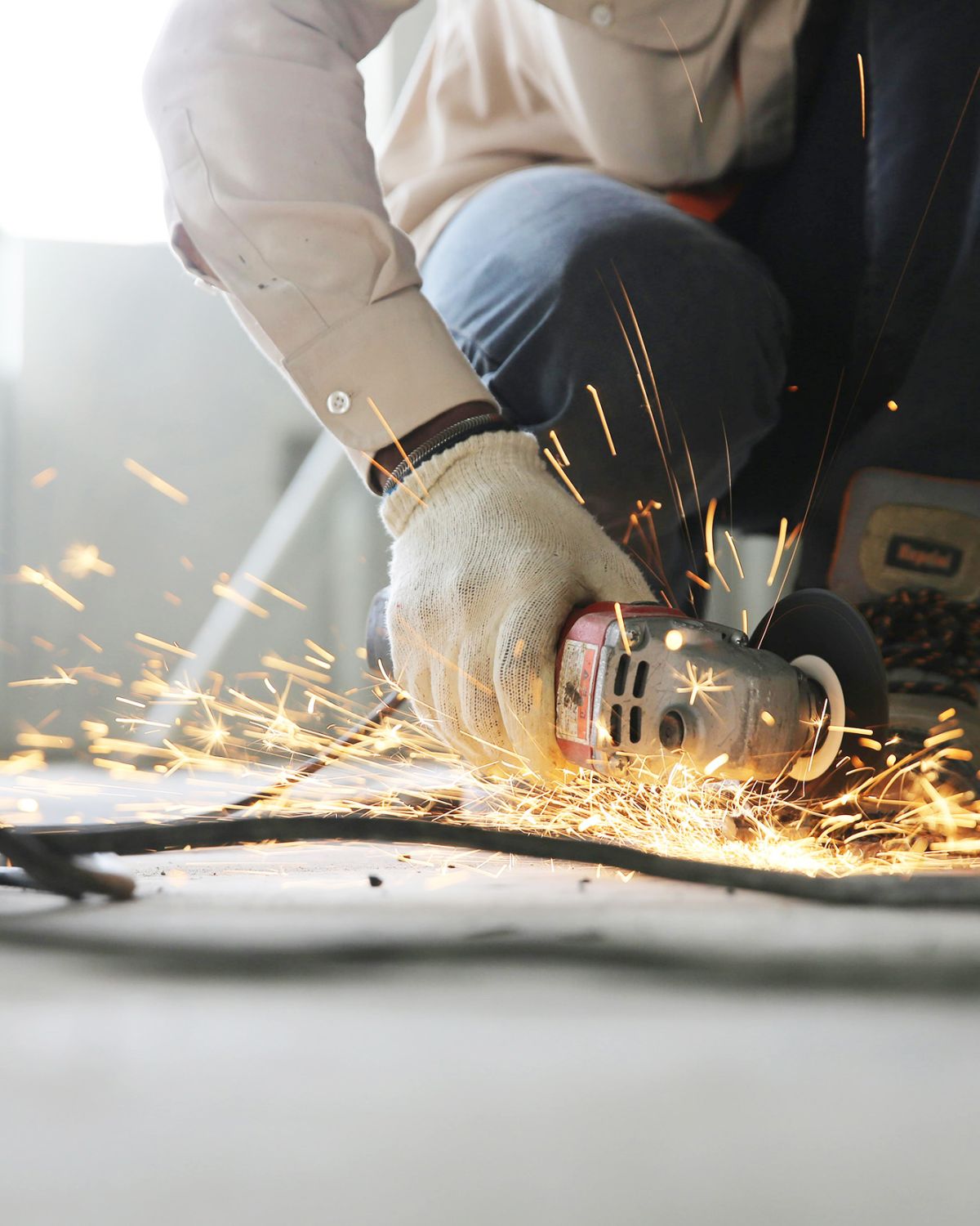 Trabajador utilizando una amoladora angular mientras saltan chispas, con ropa de protección laboral y guantes de seguridad.