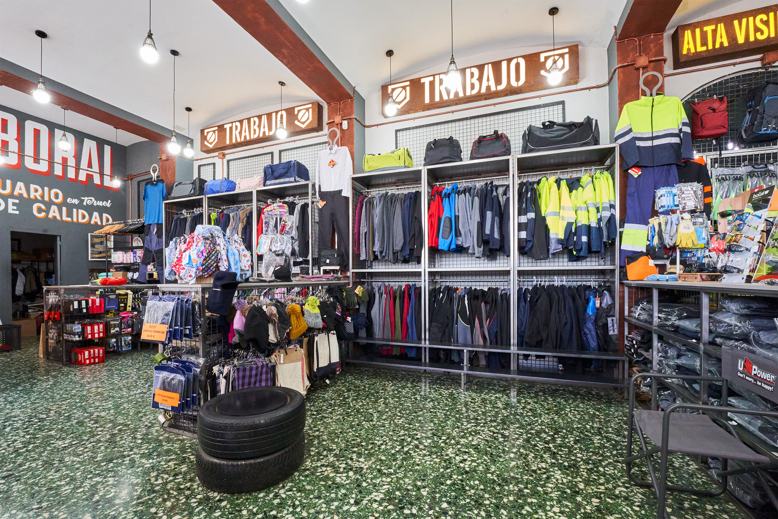 Interior de tienda de ropa laboral con chaquetas de alta visibilidad, sudaderas, mochilas, guantes y accesorios para profesionales de diversos sectores.
