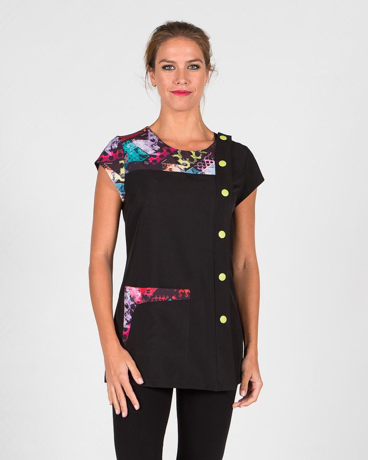 Mujer con casaca sanitaria negra con detalles multicolor en hombro y bolsillo, cierre lateral con botones verdes, posando sobre fondo blanco.