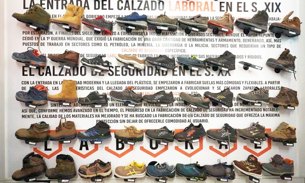 Expositor de pared con calzado laboral y de seguridad en tienda LABORAL, variedad de botas y zapatillas técnicas con descripción histórica sobre la evolución del calzado de trabajo.