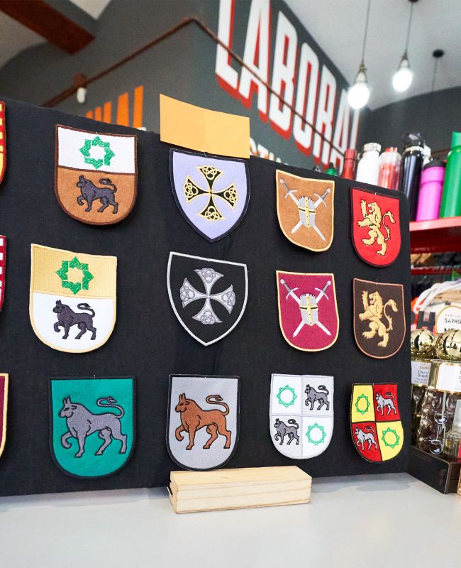 Muestrario de escudos bordados personalizados sobre mesa en tienda de ropa laboral, junto a frascos de colonia y accesorios.