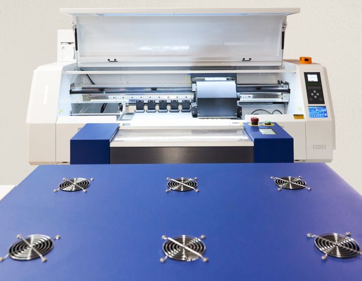 Máquina industrial de impresión DTF con bandeja frontal azul y ventiladores, utilizada para personalizar ropa laboral con alta precisión y calidad.
