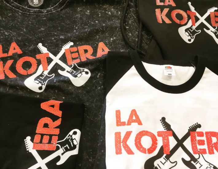 Camisetas personalizadas con diseño gráfico de “LA KOTXERA” en letras rojas y dos guitarras eléctricas cruzadas en blanco y negro. Prendas en diferentes estilos y colores (negro jaspeado, negro liso, blanco con mangas negras), listas para merchandising o eventos musicales.